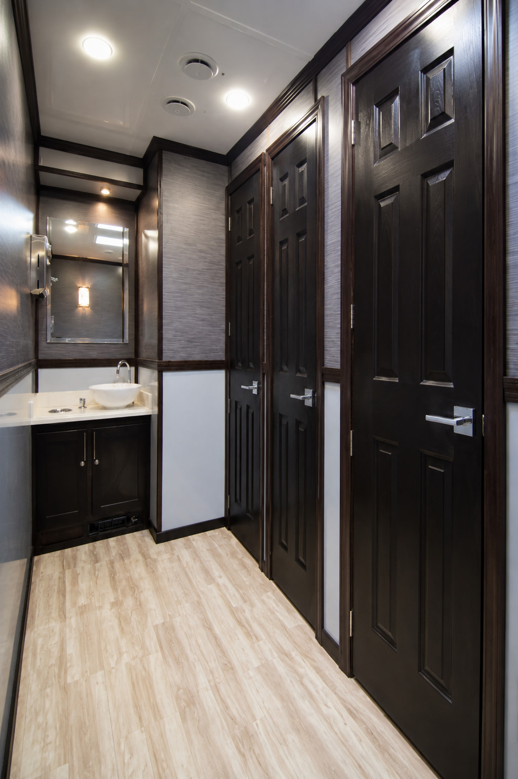 Inside a Marquee suite — a vessel basin on a solid-surface counter, chrome fittings, a framed mirror under warm sconce light, and dark panelled doors to private stalls